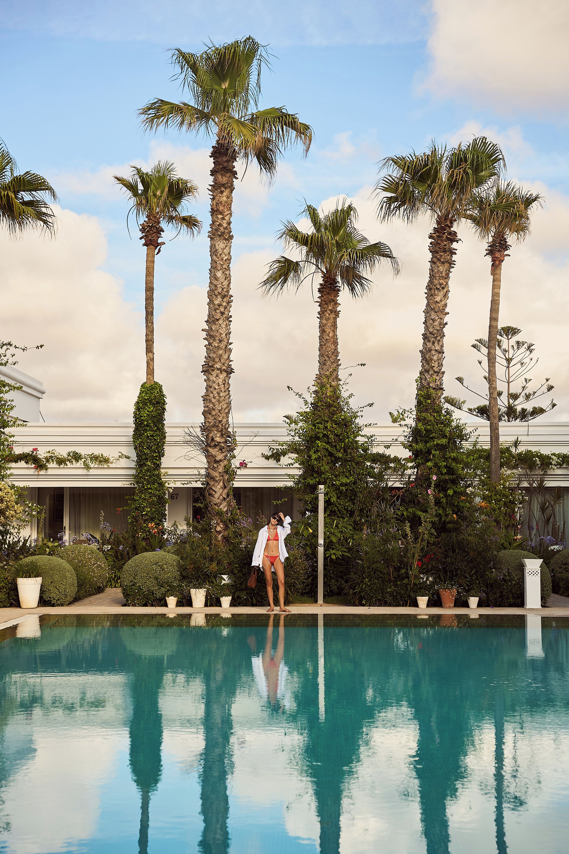 A pool area with palm trees, a building, and a person in swimwear.