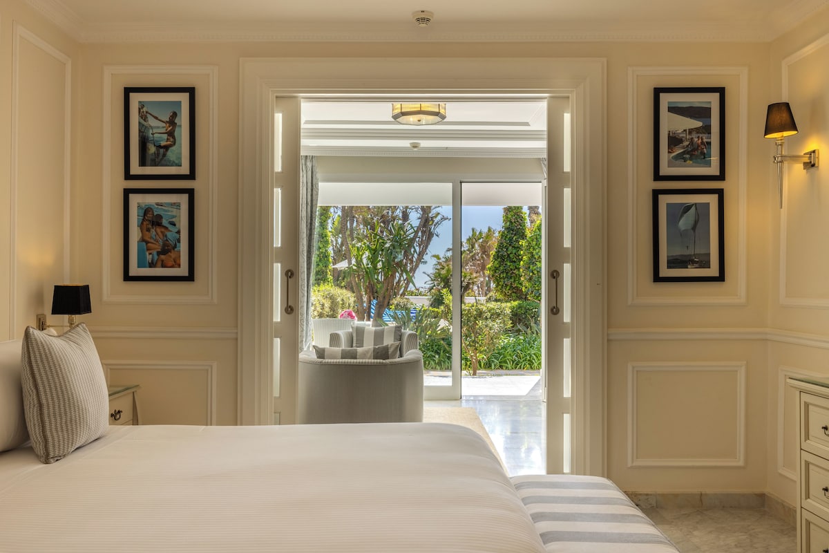 Un dormitorio con una cama grande, vistas de un jardín a través de una puerta abierta y cuadros en las paredes.