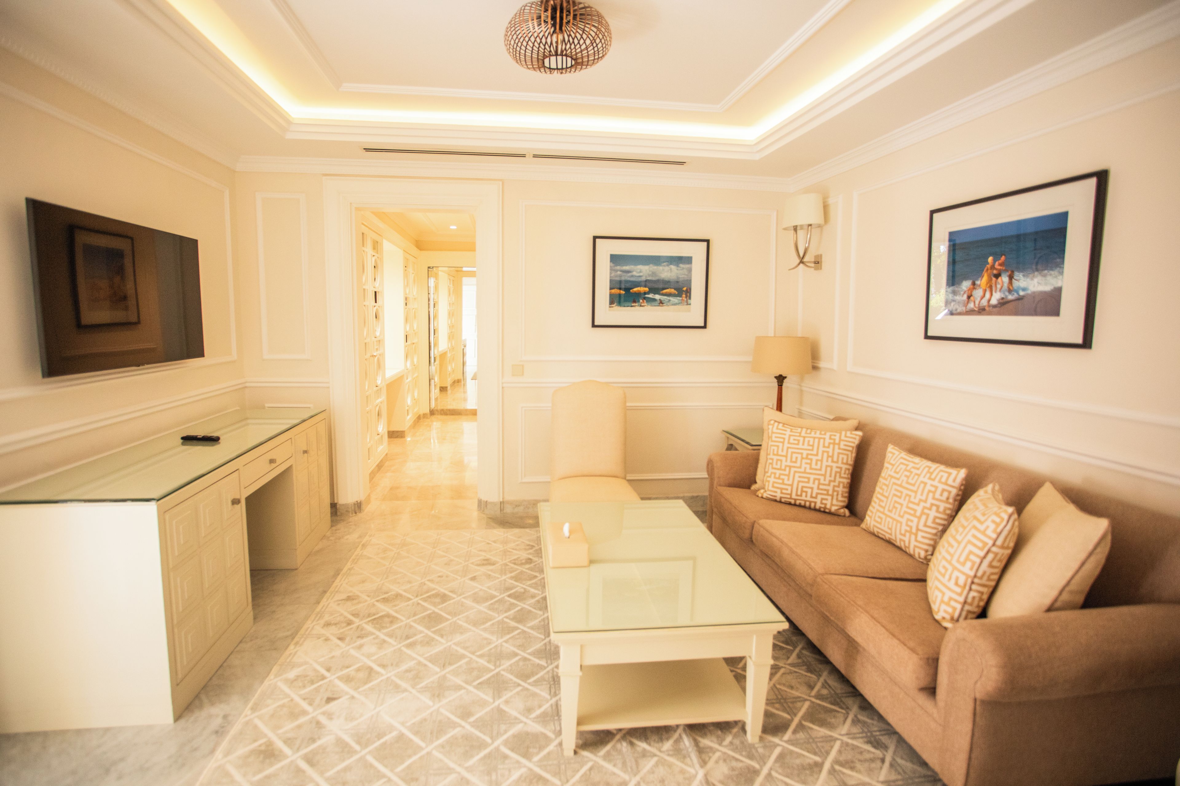 A hotel room with a sofa, a coffee table, a TV, and a painting on the wall.