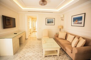 Habitación de hotel con sofá, mesa de centro, televisor y un cuadro en la pared.