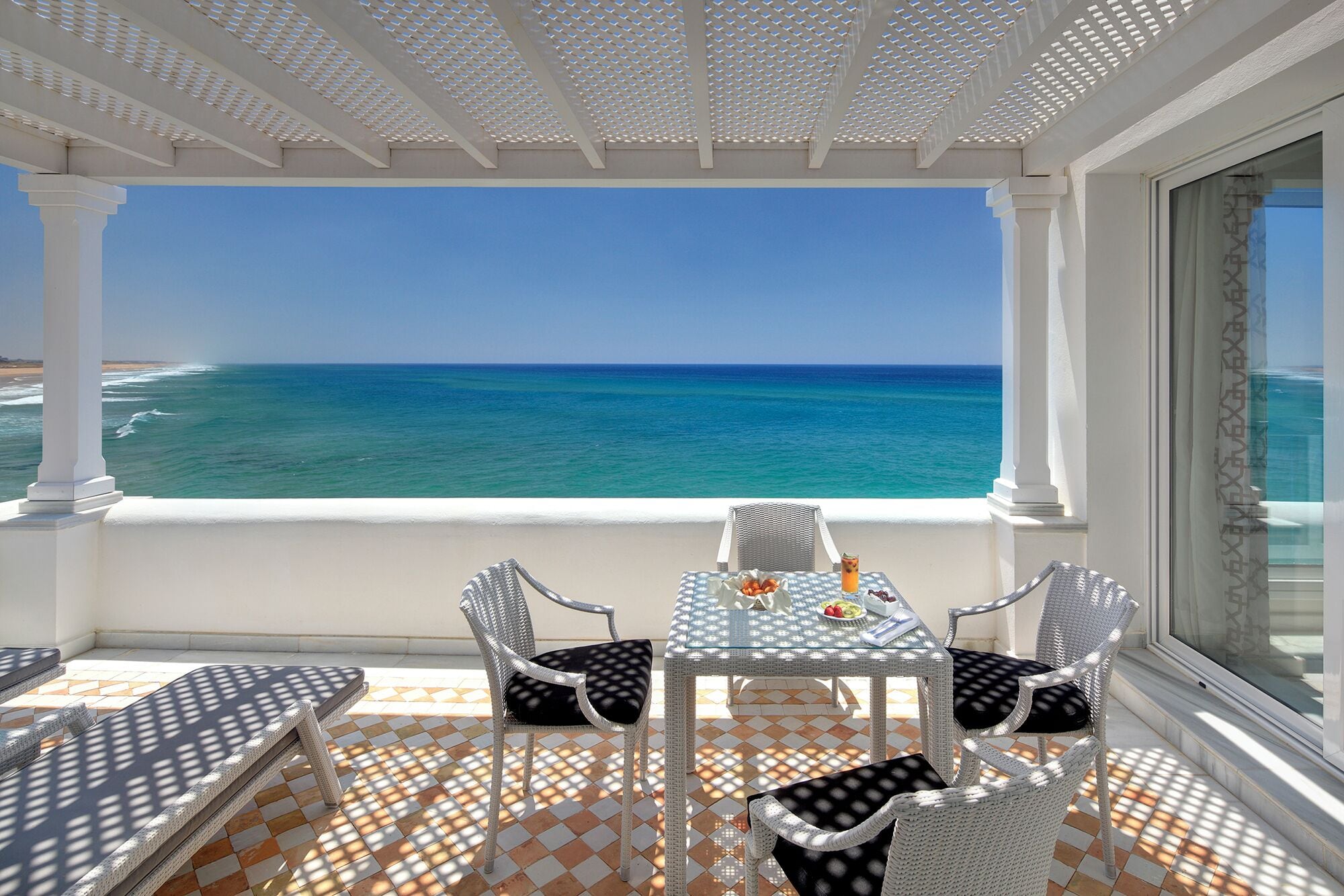 Un balcon avec une table et des chaises, donnant sur une plage et l’océan.