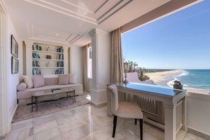 Una sala de estar moderna con una mesa de vidrio, un sofá color beige y una estantería. Un ventanal ofrece vistas a la playa y al océano.