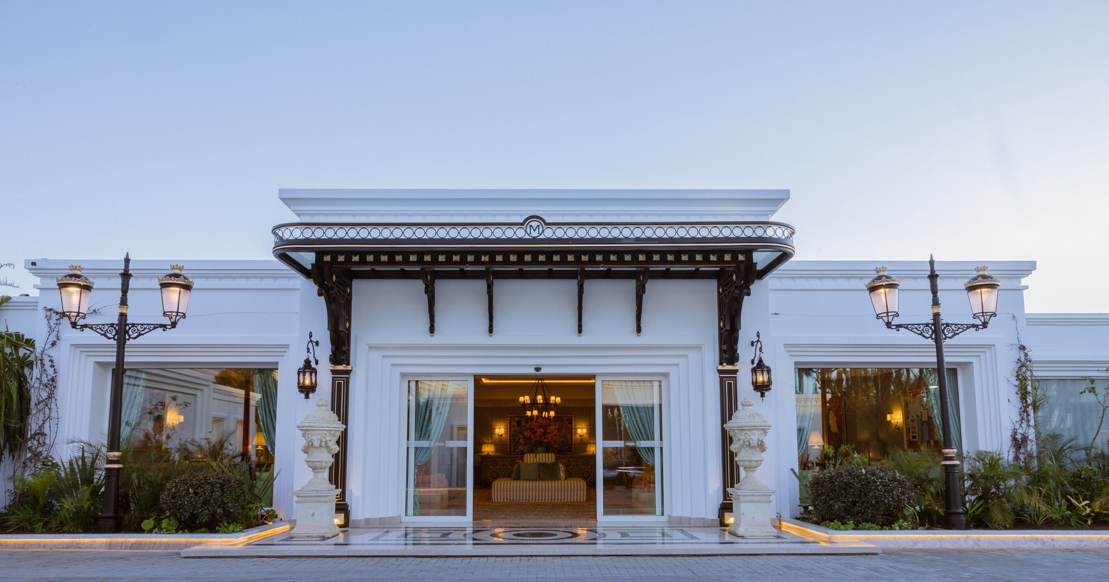 A hotel entrance with a white facade, a covered entrance, and two symmetrical street lamps.