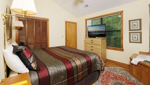 A bedroom with a bed, a television, a wooden wardrobe, a window with a view of trees, and a ceiling fan. - The Bird Hallar - Cozy, quiet cabin in The Glades! (Gatlinburg)