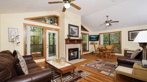 A spacious living room with a fireplace, wooden flooring, and a ceiling fan. - The Bird Hallar - Cozy, quiet cabin in The Glades! (Gatlinburg)