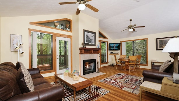 A spacious living room with a fireplace, wooden flooring, and a ceiling fan. - The Bird Hallar - Cozy, quiet cabin in The Glades! (Gatlinburg)