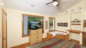A bedroom with a bed, a television, a wooden dresser, a bathtub, and a ceiling fan. - The Bird Hallar - Cozy, quiet cabin in The Glades! (Gatlinburg)