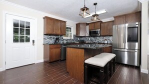 A modern kitchen with wooden cabinets, a stainless steel refrigerator, a microwave, and a bar stool. - Whiskey Ridge - Pet-friendly, Game Tables ,Wi-Fi, Firepit, Rocking Chairs (Sevierville)