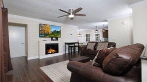 A spacious living room with a fireplace, leather sofa, and a television mounted above it. - Whiskey Ridge - Pet-friendly, Game Tables ,Wi-Fi, Firepit, Rocking Chairs (Sevierville)