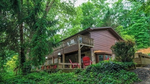 A cabin with a wooden deck, a porch, and a stone foundation. - Whiskey Ridge - Pet-friendly, Game Tables ,Wi-Fi, Firepit, Rocking Chairs (Sevierville)