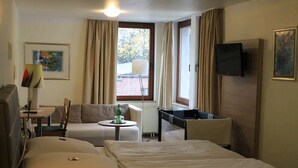 Habitación de hotel con dos camas, un escritorio, una silla, un televisor y una ventana con cortinas.