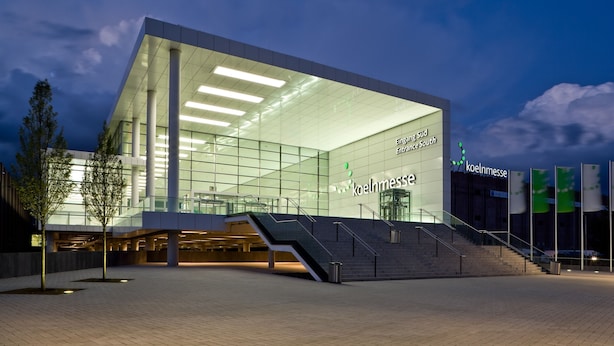 Un edificio moderno con fachada de vidrio, una escalera que conduce a la entrada y el nombre 'koelnmesse' visible en grande.