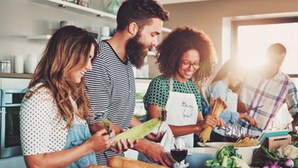 Un grupo de personas en una cocina preparando comida con pan, verduras y un bol de salsa.