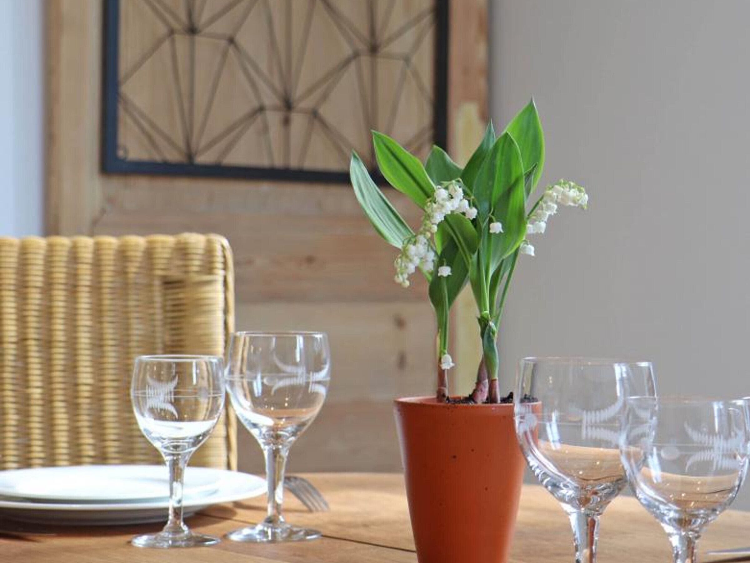 A dining table with a potted plant and four empty wine glasses.
