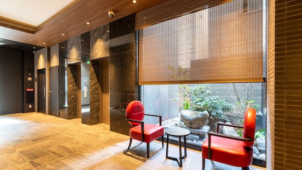 Eine moderne Lobby mit einem großen Fenster, zwei roten Sesseln und einem kleinen Tisch.