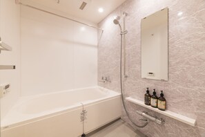 Ein modernes Badezimmer mit einer großen Badewanne, einer Handbrause, einem wandmontierten Spiegel und einem Ablagefach für Toilettenartikel.