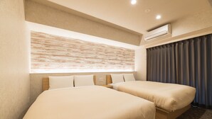 Ein Hotelzimmer mit zwei Betten, einer großen Wandklimaanlage und einem mit Vorhängen versehenen Fenster.