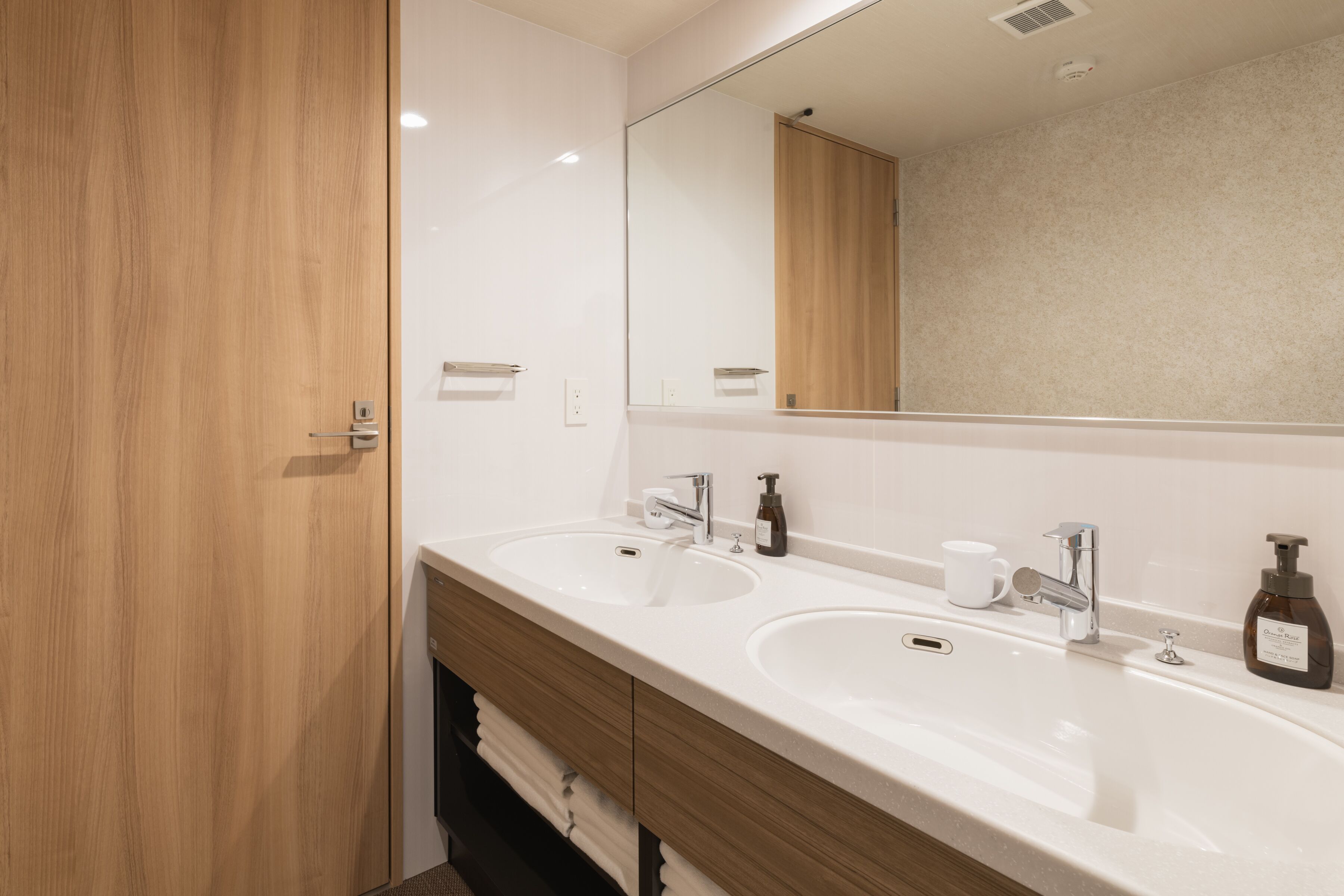 A modern bathroom with two sinks, a large mirror, and wooden cabinetry.
