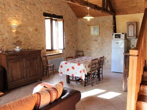 A rustic kitchen with stone walls, wooden furniture, a dining table with a floral tablecloth, and a white refrigerator.