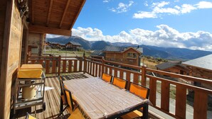 Un terrazzo in legno con tavolo e sedie, affacciato su un paesaggio montuoso con diverse case.