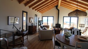 Un ampio soggiorno con soffitto in legno, un tavolo da pranzo con sedie, un divano e un'ampia finestra che si affaccia sulla città.