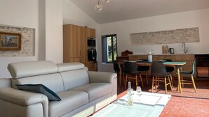 Una sala de estar moderna con sofá, mesa de comedor y sillas. Cuenta con una zona de cocina con lavaplatos y armarios.