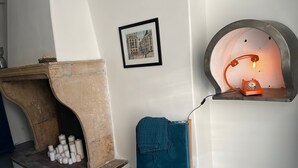 A room with a stone fireplace, a blue chair, a framed picture, and a vintage rotary phone. - Gîte Dans un Mas Provencal Avec Piscine, 3km du Centre de L'isle-sur-la-sorgue (L'Isle-sur-la-Sorgue)