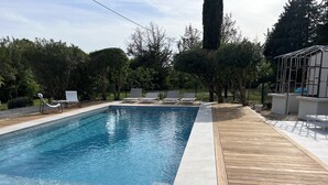 Una piscina rectangular con agua azul cristalina, rodeada por una terraza de madera y sillas de descanso.