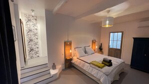 Un dormitorio con cama, lámparas de noche, una lámpara colgante, una ventana y una escalera.