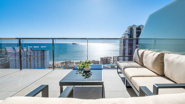 A balcony with a view of the sea, a sofa, a table with a plant, and a glass railing. - Sunset Waves 18-35 Poniente Beach Resort (Benidorm)