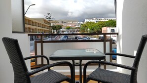 A balcony with wicker chairs and a small table, overlooking a parking area and buildings. - Best Location. Playa Las Vistas. Free Wifi (Playa de la Américas)