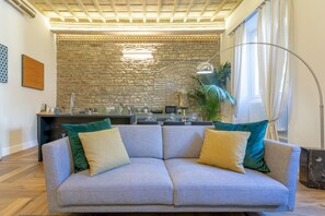 A modern living room with a grey sofa, a stone wall, and a kitchen in the background.