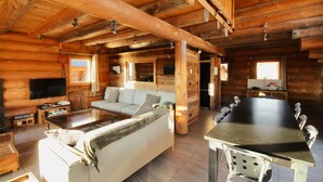 Interior de una cabaña de troncos con sala de estar, sofá, mesa de comedor y sillas.