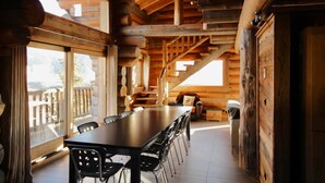 Un interior de madera con una larga mesa de comedor, sillas y una escalera que lleva a un nivel superior.