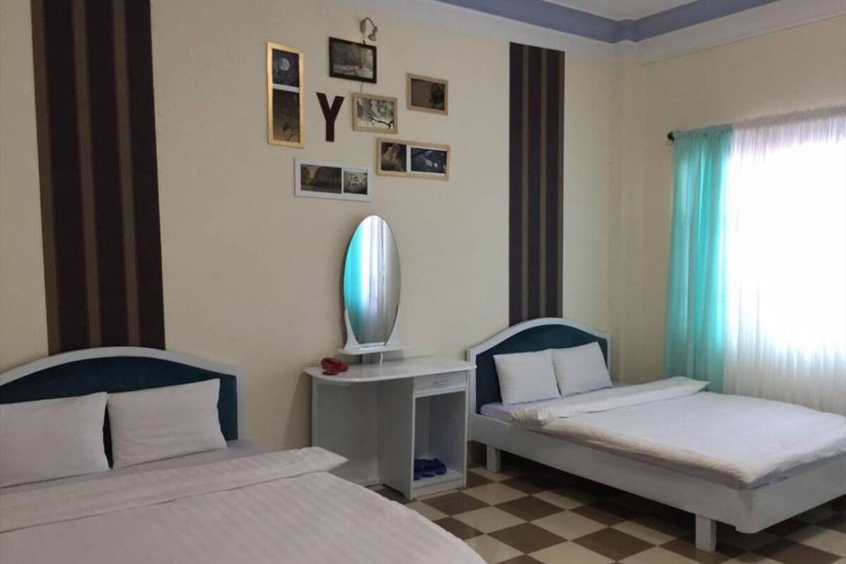 A hotel room with two beds, a small desk, and a wall decorated with framed pictures and letters.
