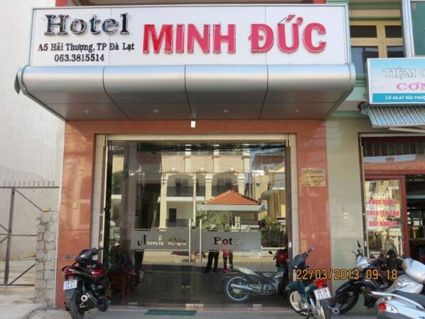 A hotel entrance with a sign reading "MINH DUC" and a contact number.
