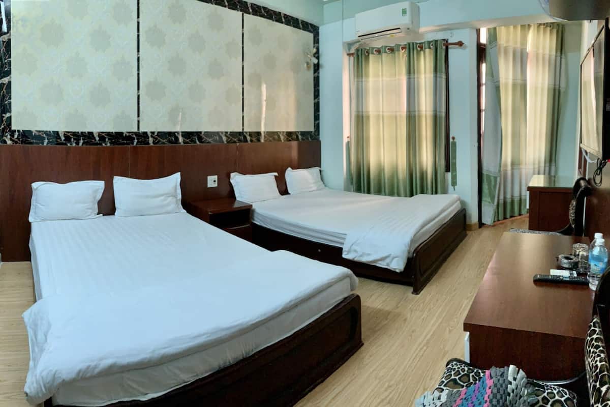A hotel room with two beds, a wooden desk, a chair, a TV, and a window with curtains.