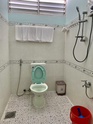 A bathroom with a toilet, shower, and a red bucket.