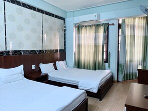 A hotel room with two beds, a wooden headboard, a large mirror, an air conditioning unit, and a window with green curtains.