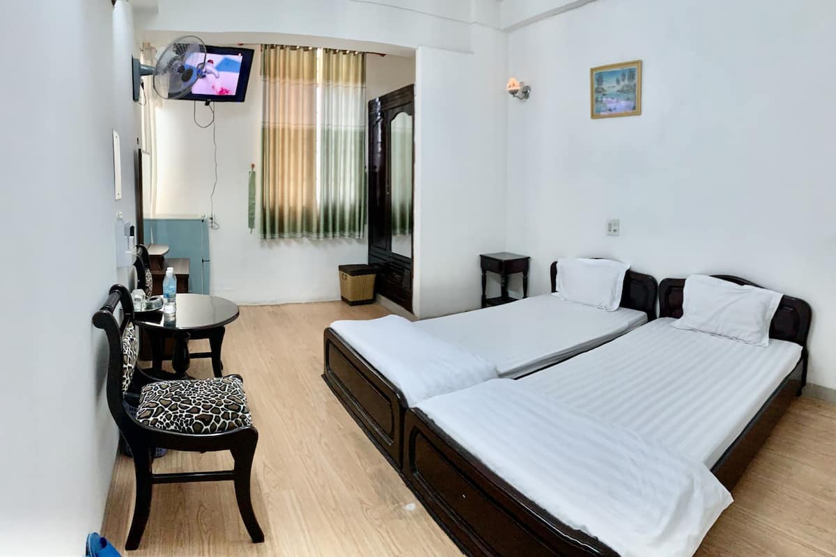A hotel room with a bed, a chair, a small table, a TV, and a window with curtains.
