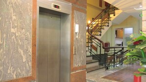 Ein Aufzug mit digitaler Anzeige, Marmorwänden, einer Treppe mit Metallgeländer und einer Zimmerpflanze.