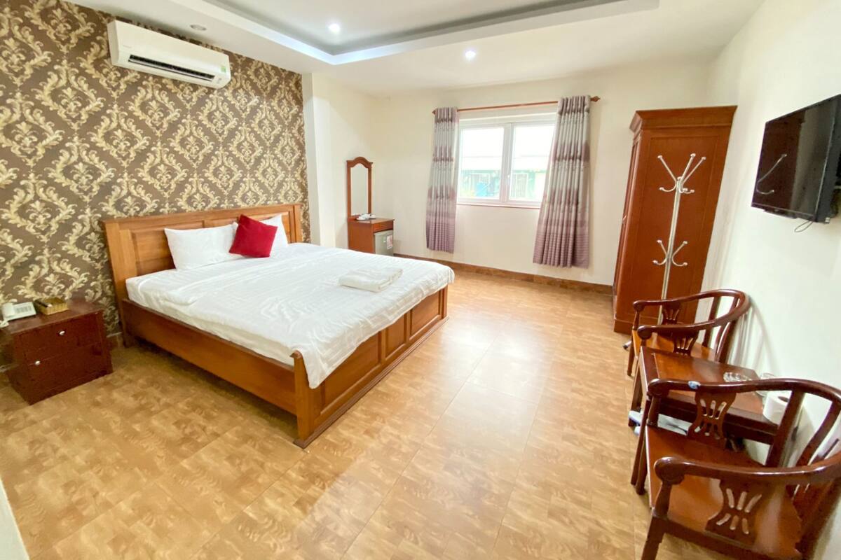 Une chambre d’hôtel avec un grand lit, un plancher en bois, une armoire, une télévision et une fenêtre avec des rideaux.