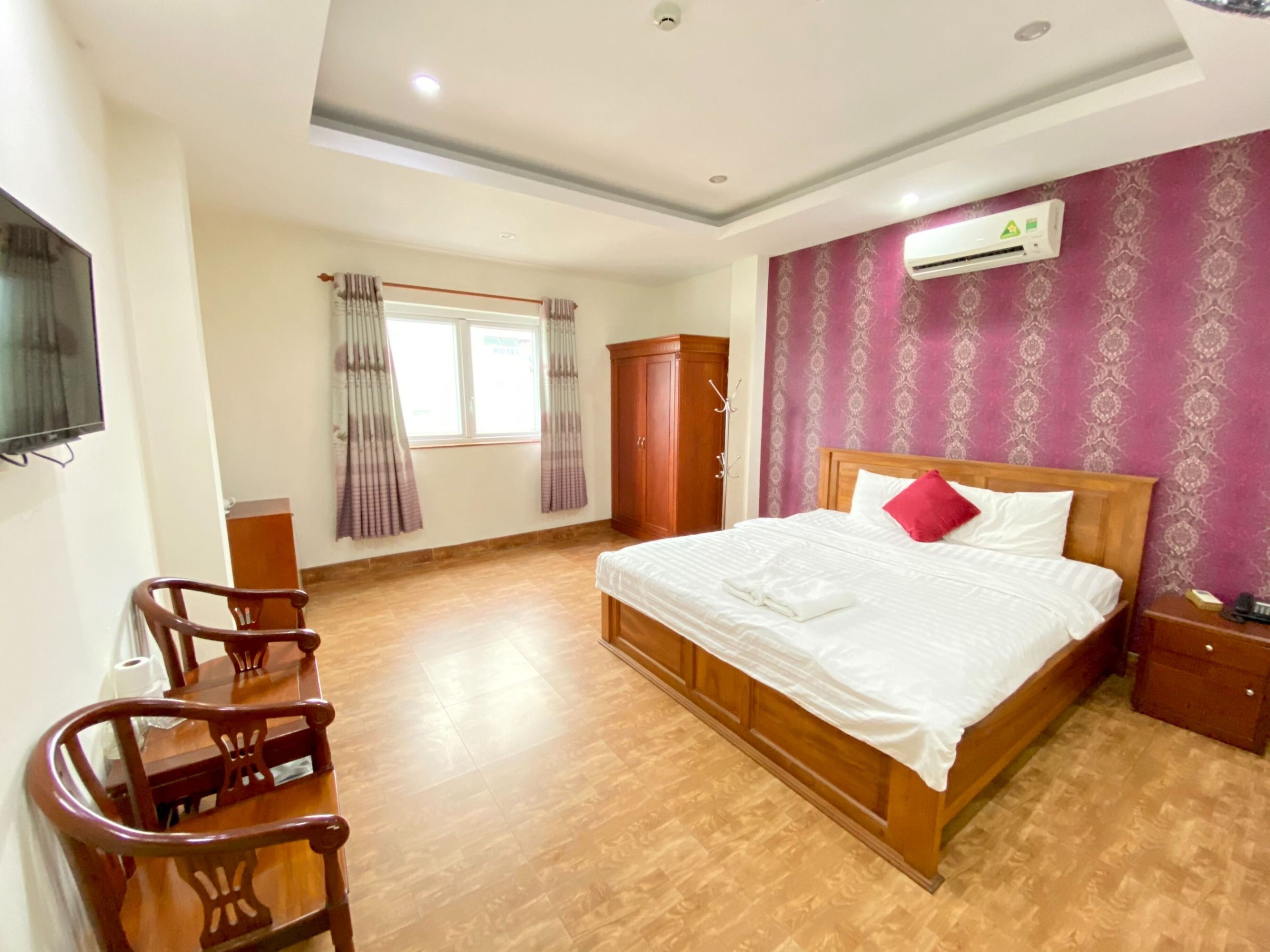 Une chambre d’hôtel avec un lit en bois, un bureau, une chaise, une armoire et un appareil de climatisation fixé au mur.