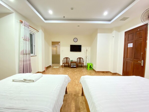 Habitación de hotel con dos camas, piso de madera, televisor de pantalla plana montado en la pared y una puerta a la derecha.