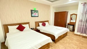 Ein Hotelzimmer mit zwei Holzbetten, weißen Laken und roten Kissen. Ein kleiner Nachttisch mit Telefon und einer grünen Leuchte befindet sich über dem Bett. Im Hintergrund sind ein Holzschrank und ein Spiegel zu sehen.