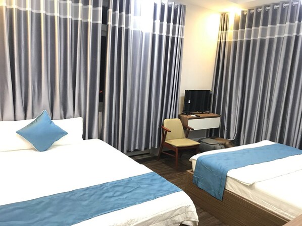 A hotel room with two beds, a desk with a computer, a chair, and grey curtains.