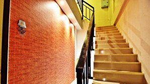 Uma escadaria com uma parede de tijolos de um lado e uma parede amarela do outro, que leva a um andar superior.