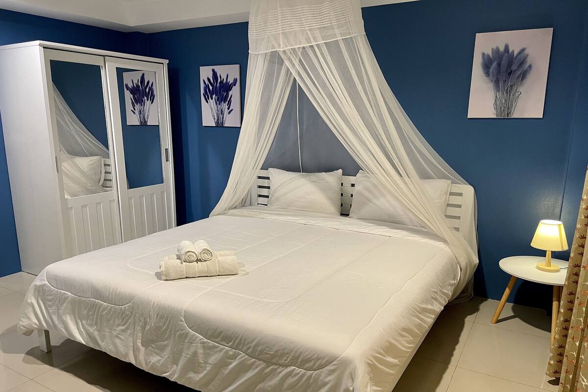 A neatly made bed with white linens, a white canopy, and a small bedside table with a lamp.