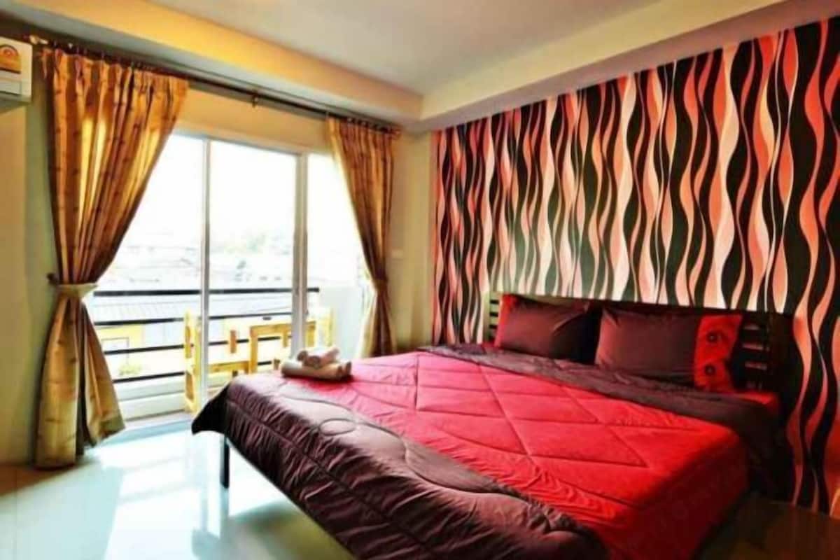 A hotel room with a large bed, a view of the outdoors, and a patterned wall.