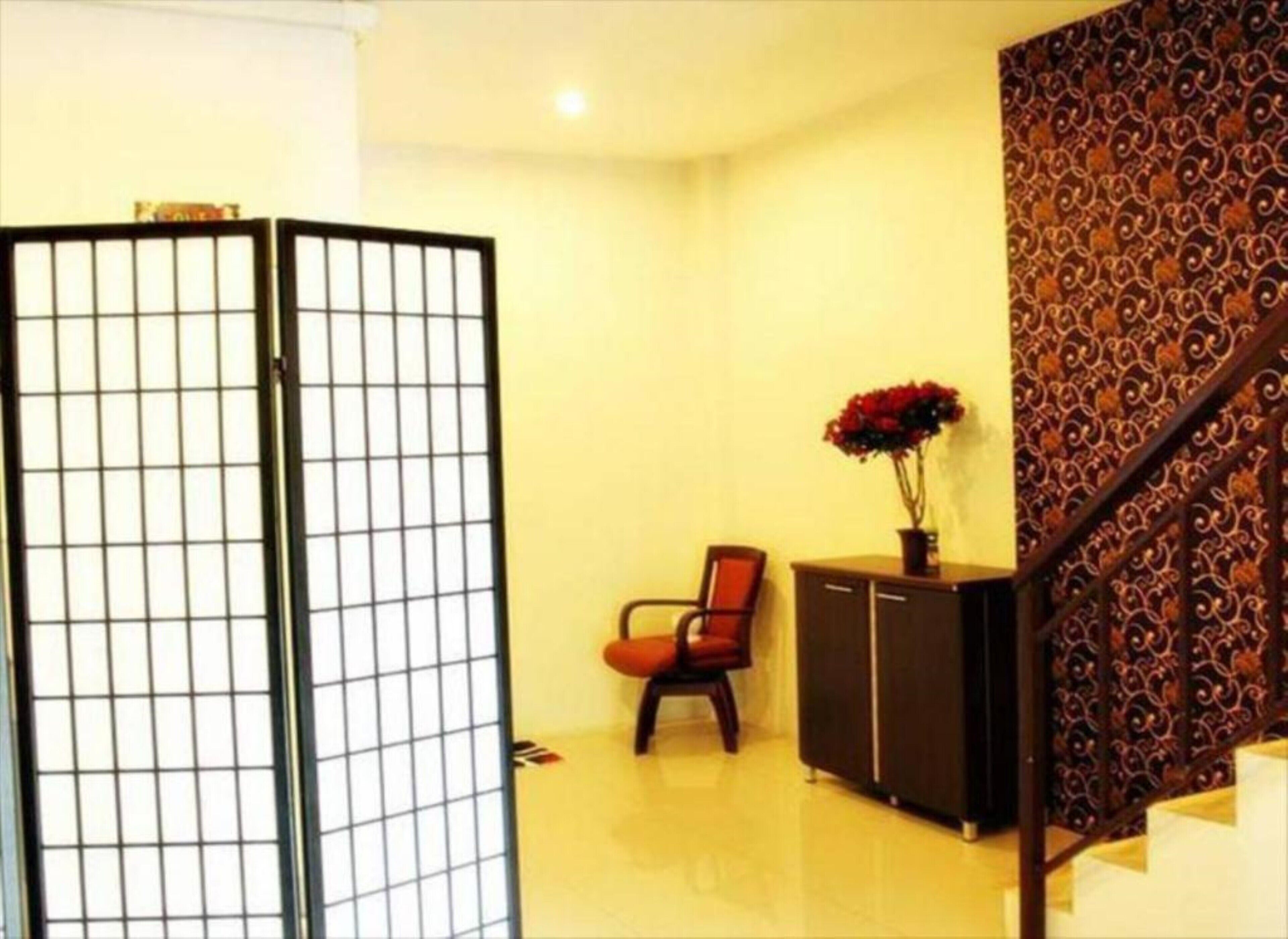A room with a traditional sliding door, a chair, a cabinet, and a staircase with patterned wallpaper.